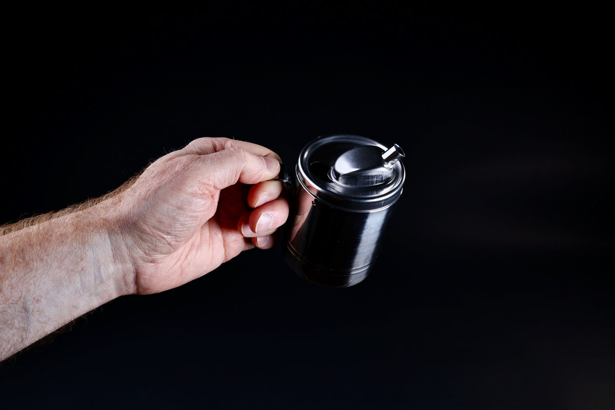 Stainless steel oil cruet small — held by handle in upright position showing full body and spout from above