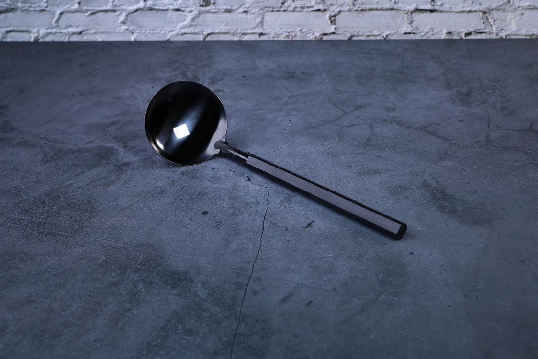 Stainless steel oxidized ladle — full view showing blackened solid bowl, ferrule, and wooden handle