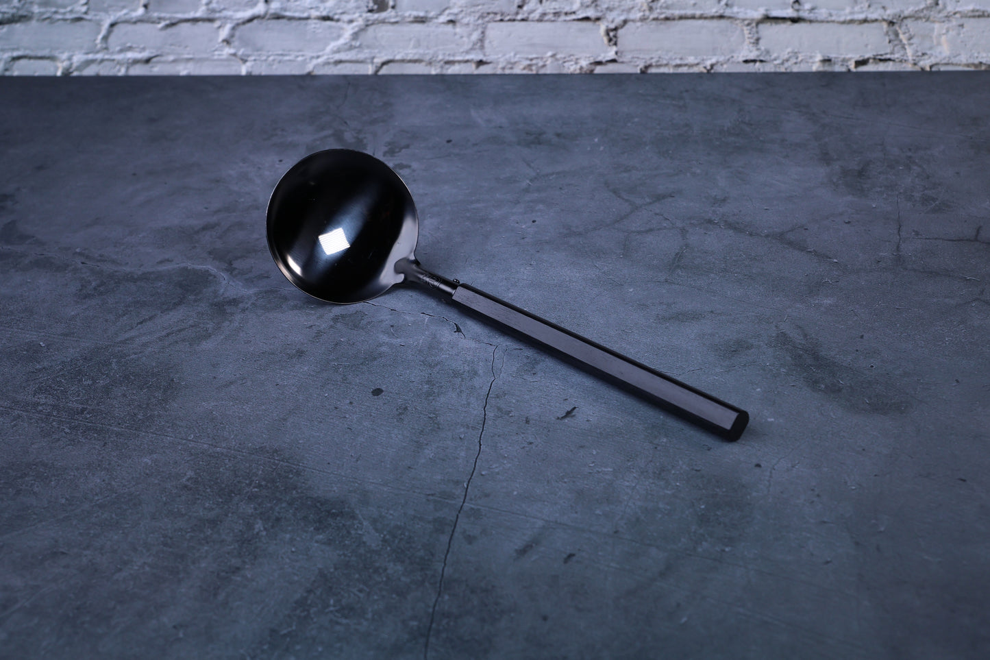 Stainless steel oxidized ladle — full view showing blackened solid bowl, ferrule, and wooden handle