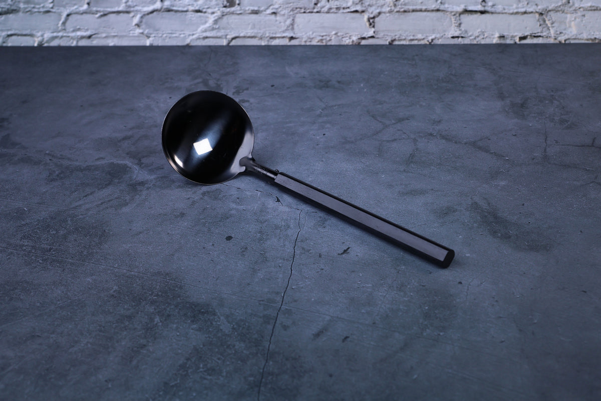 Stainless steel oxidized ladle — full view showing blackened solid bowl, ferrule, and wooden handle