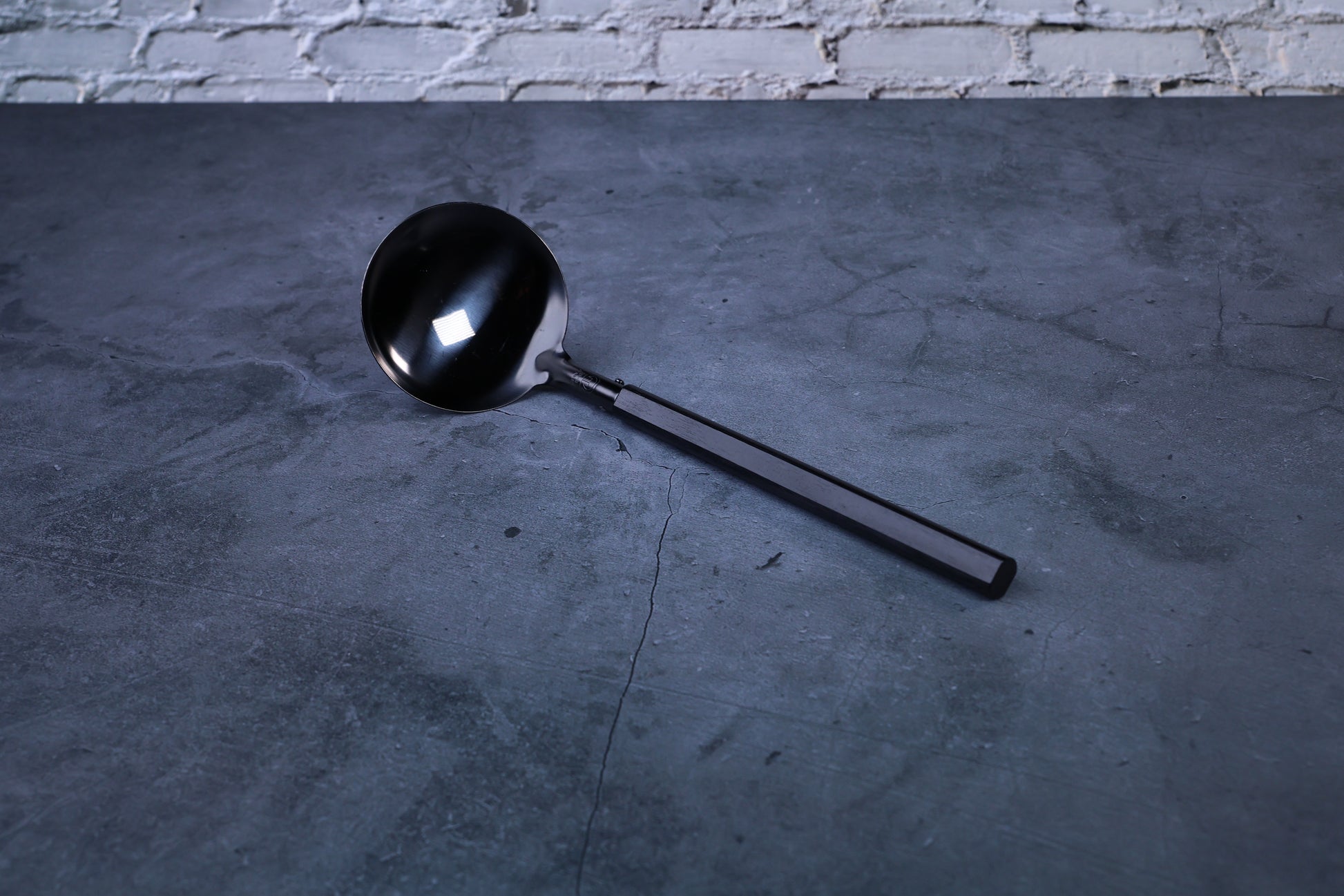 Stainless steel oxidized ladle — full view showing blackened solid bowl, ferrule, and wooden handle