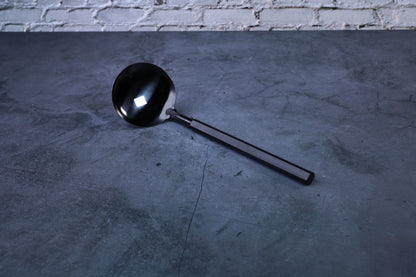 Stainless steel oxidized ladle — full view showing blackened solid bowl, ferrule, and wooden handle