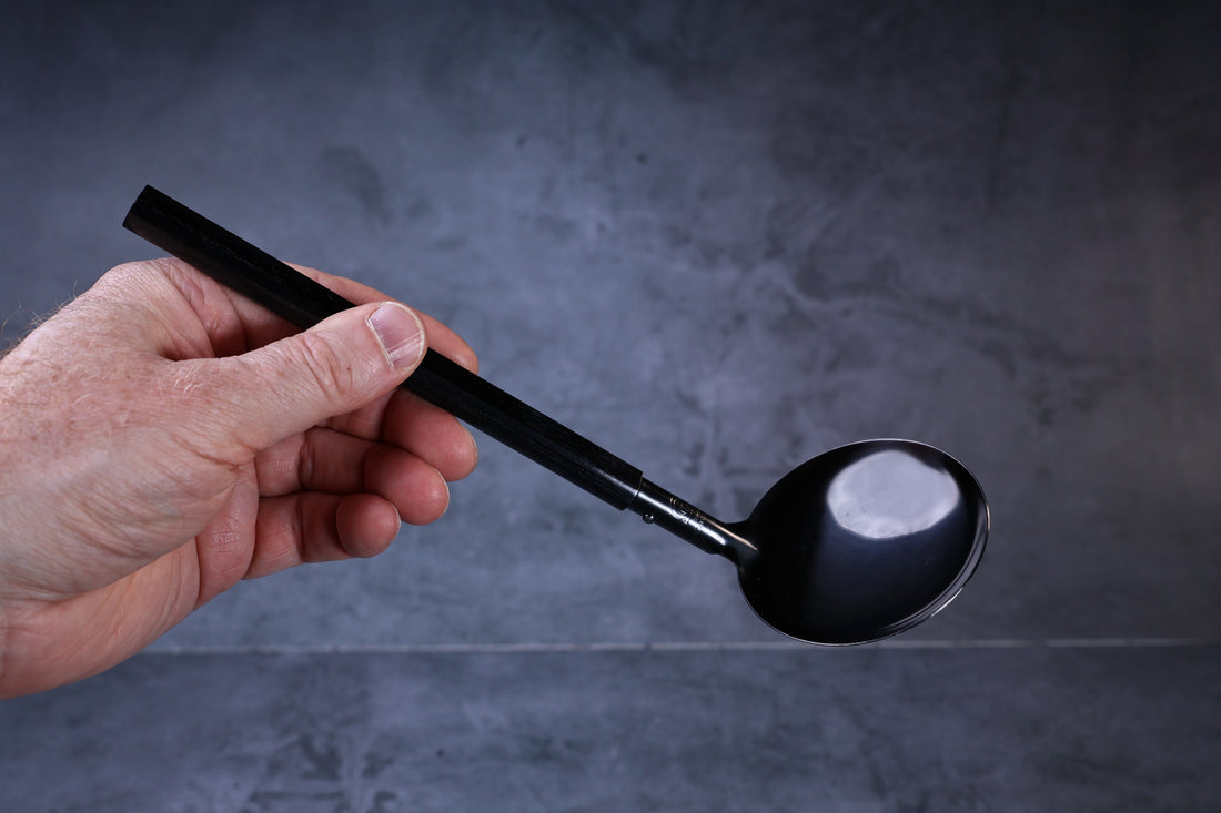 Stainless steel oxidized ladle — octagonal wooden handle grip and solid blackened bowl held in hand