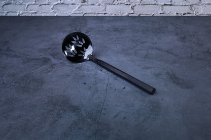 Stainless steel oxidized perforated ladle — full view showing blackened bowl, perforations, and wooden handle