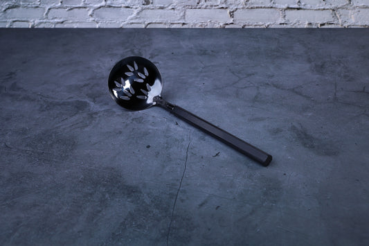 Stainless steel oxidized perforated ladle — full view showing blackened bowl, perforations, and wooden handle