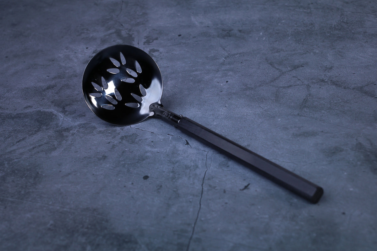 Stainless steel oxidized perforated ladle — close view of blackened perforated bowl and handle