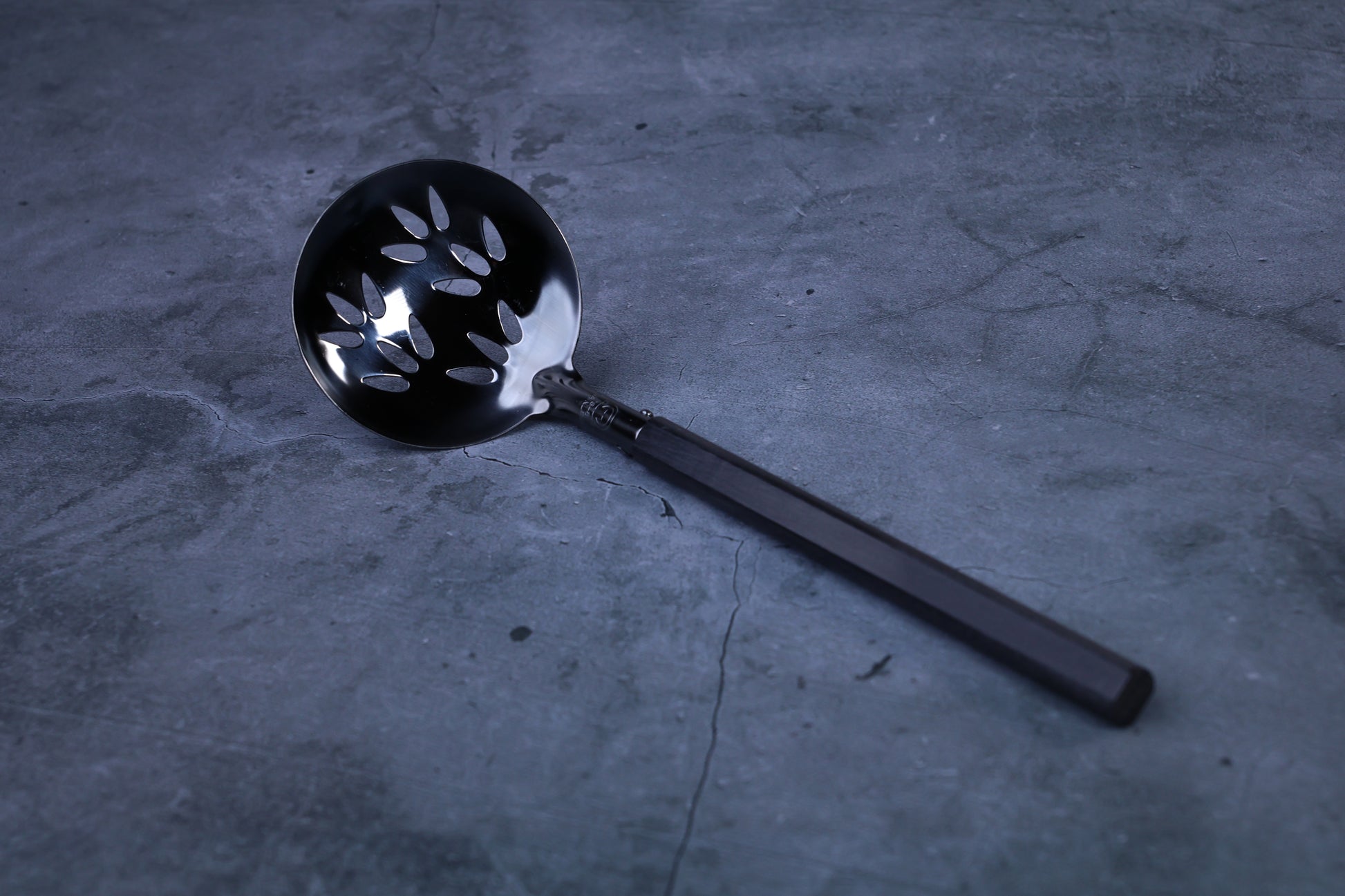 Stainless steel oxidized perforated ladle — close view of blackened perforated bowl and handle