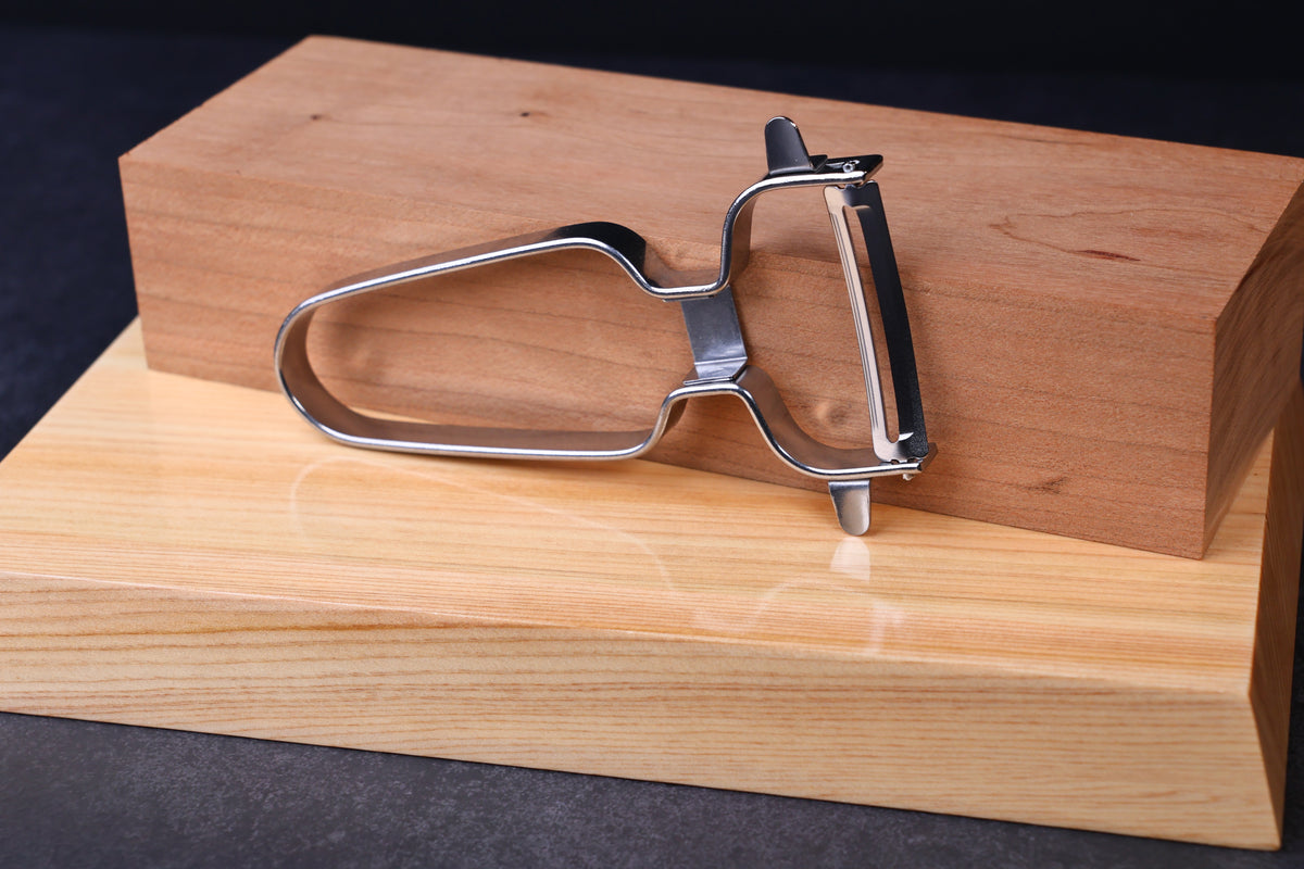 Stainless steel vegetable peeler — handle loop shape and blade side profile showing swivel mechanism on wood surface