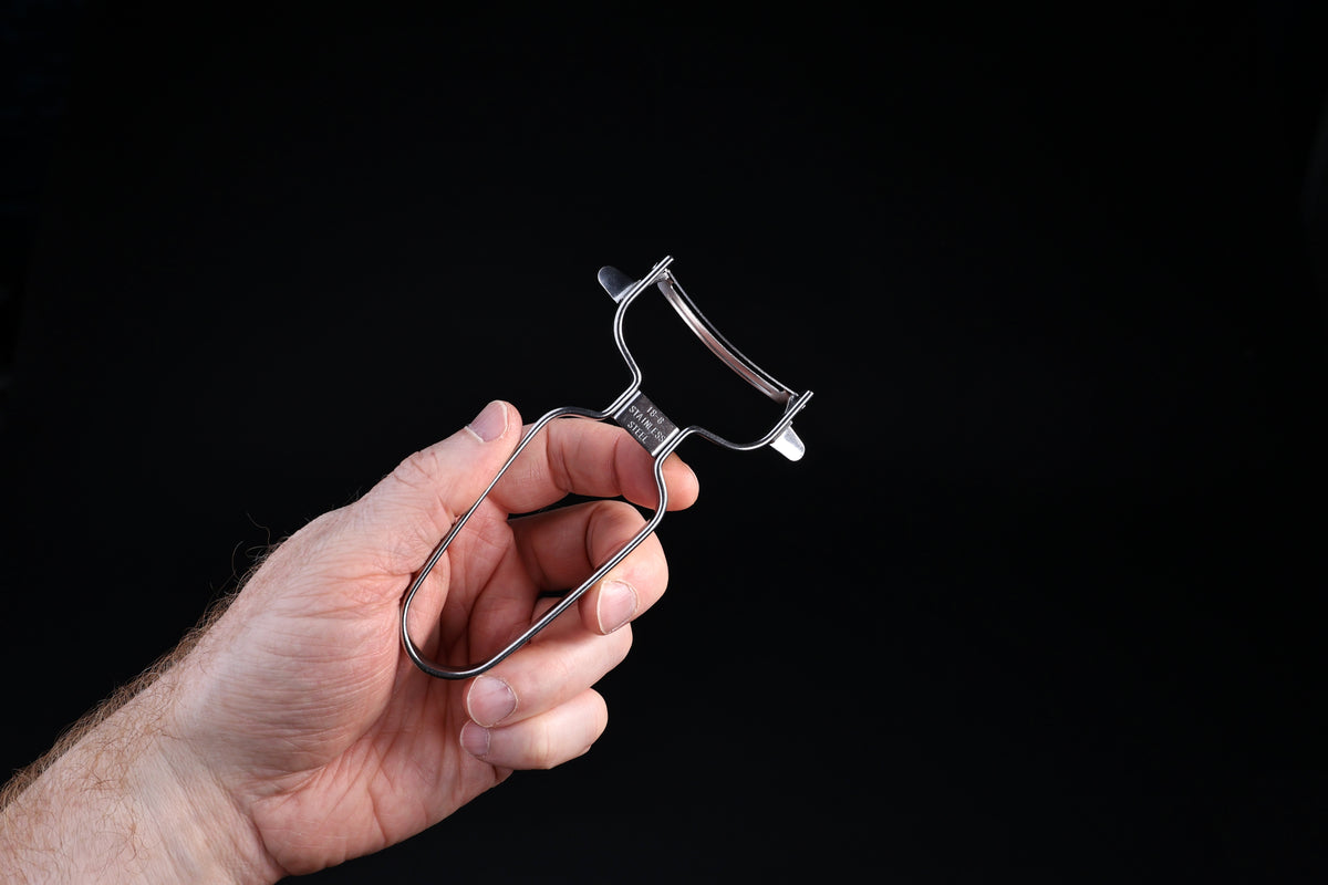Stainless steel vegetable peeler — wire frame handle, swivel blade, and 18-8 stainless stamp held in hand
