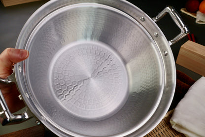 hand holding close up interior of two handled stepped aluminum silvery pot with shiny hammered surface