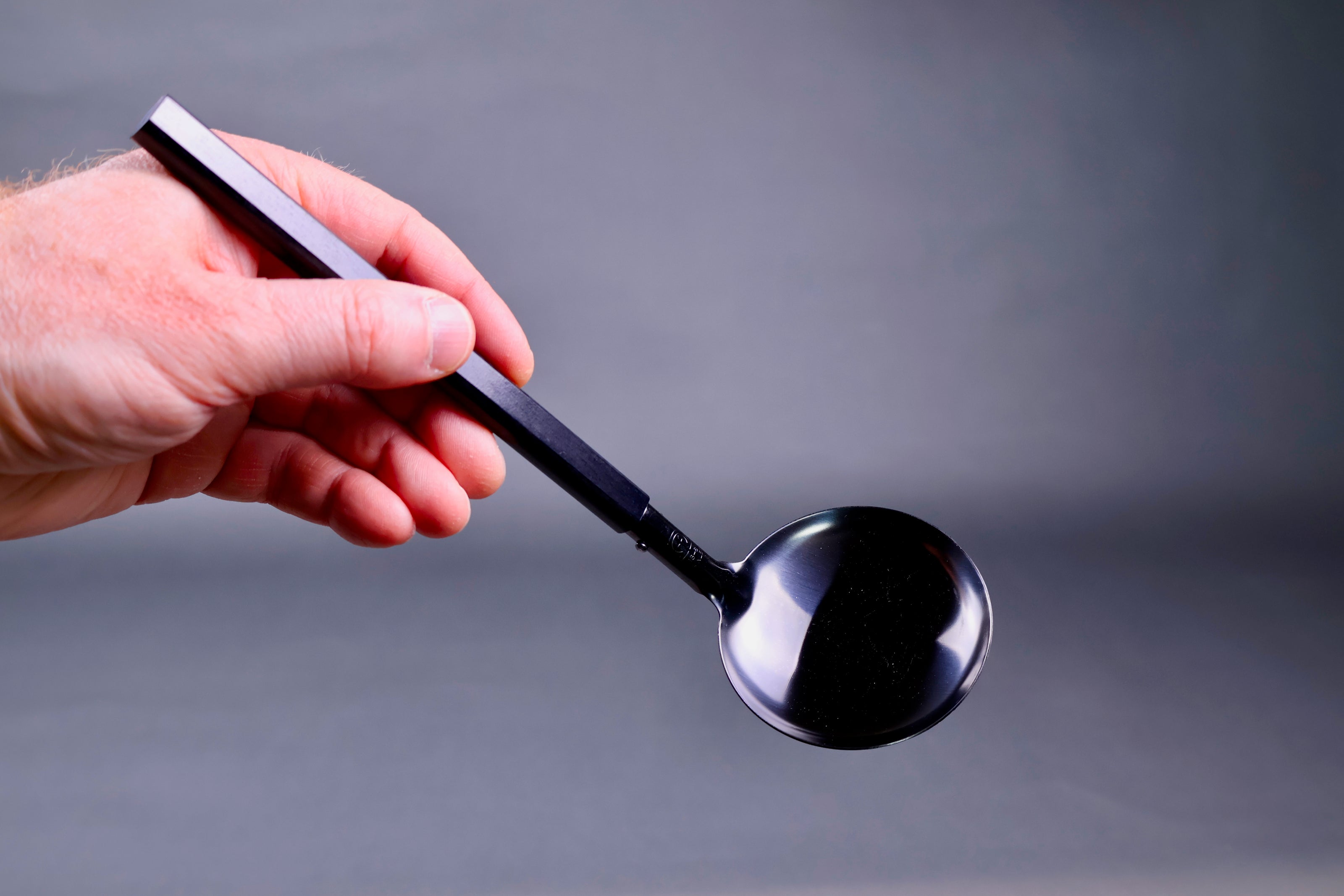 hand holding darkened steel solid ladle with dark wood handle in grey backdrop