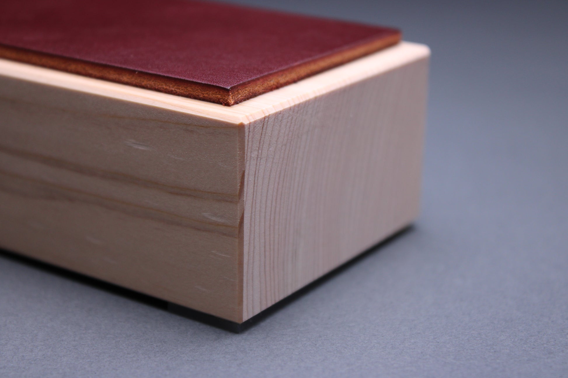 thick strip English bridle leather showing unique burgundy espresso brown color and natural leather color atop tall sturdy hinoki wood base and light grey background detailed closeup