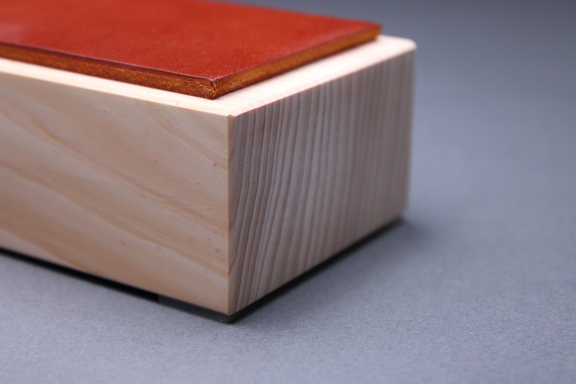 thick strip English bridle leather showing unique ochre tan brown color and natural leather color atop tall sturdy hinoki wood base and light grey background detailed closeup