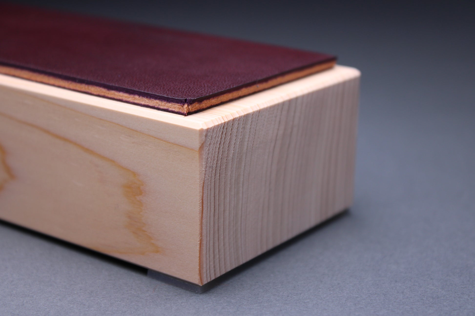 thick strip English bridle leather showing unique purple plum color and natural leather color atop tall sturdy hinoki wood base and light grey background detailed closeup