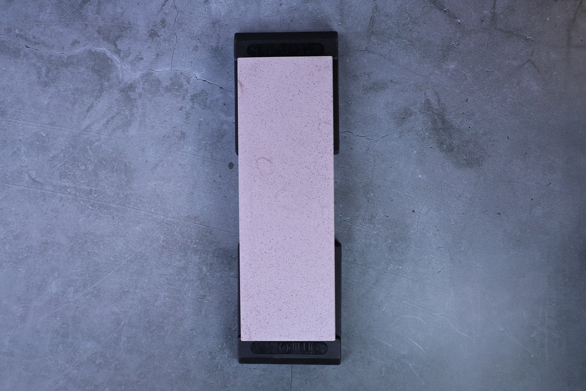 Pale ceramic whetstone fully seated in Suehiro rubber base, straight overhead view showing full stone surface