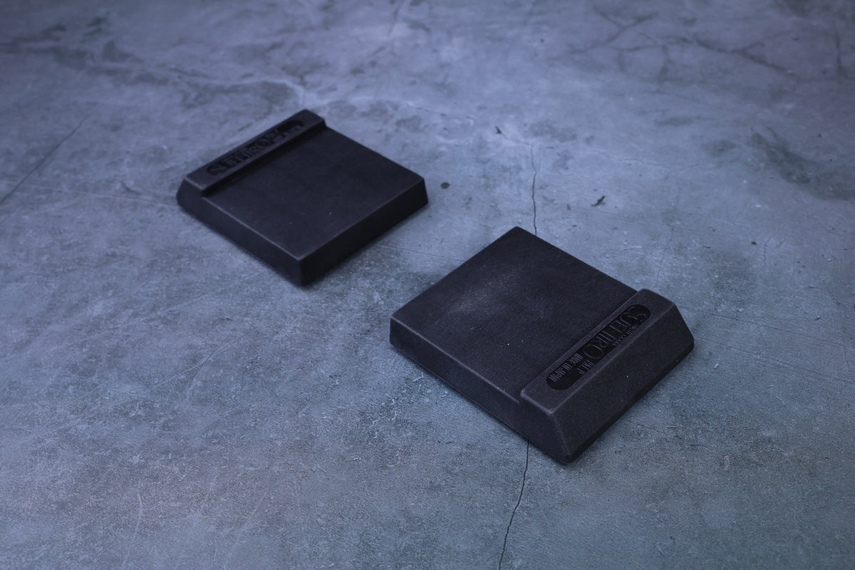 Two Suehiro rubber whetstone bases angled on concrete, showing wedge profile and relative size difference
