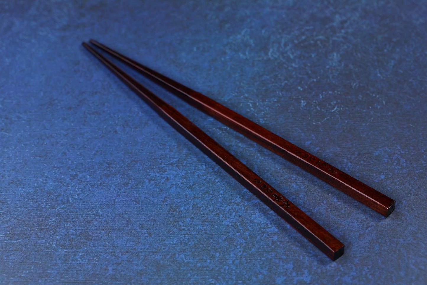 Suri Urushi Hinoki chopsticks 22cm laid flat on blue surface showing full length and Japanese engraving