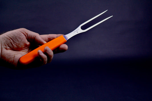hand holding two pronged metal caring fork with orange plastic handle in dark bluish background