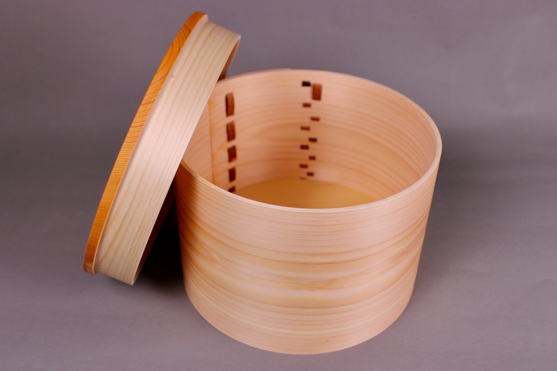 round hinoki wood container with lid leaning on wood body natural wood tone and appearance in dark grey background