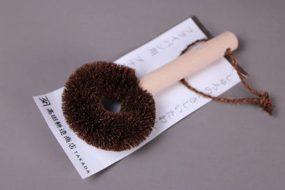 tawashi wood handled with hanging loop for coarse scrubber for cooking pans atop brand label with grey background