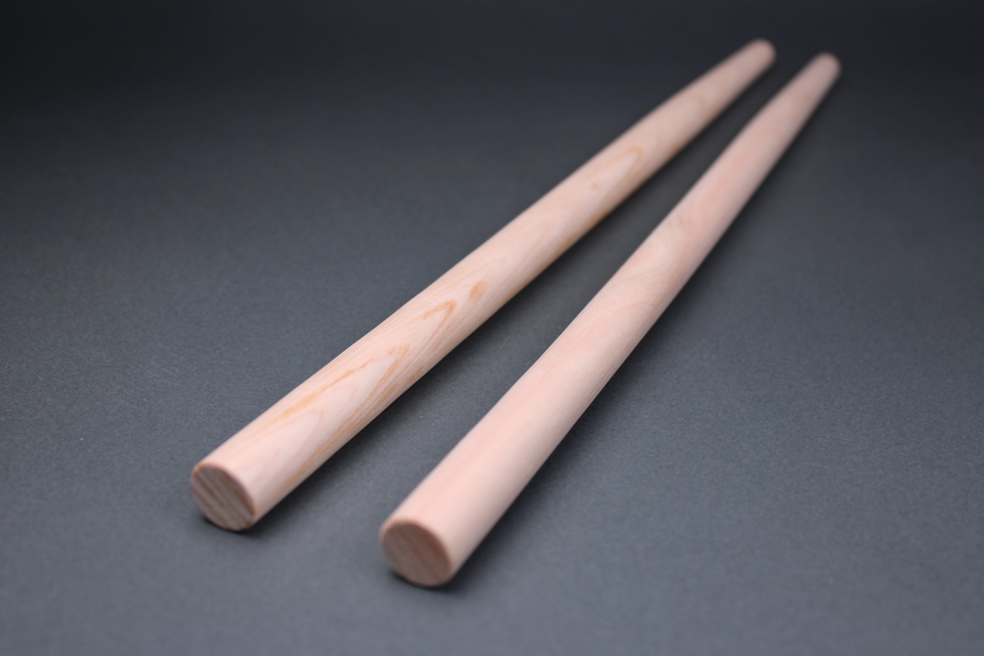 long thick round hinoki wood cooking chopsticks sit parallel on dark grey background