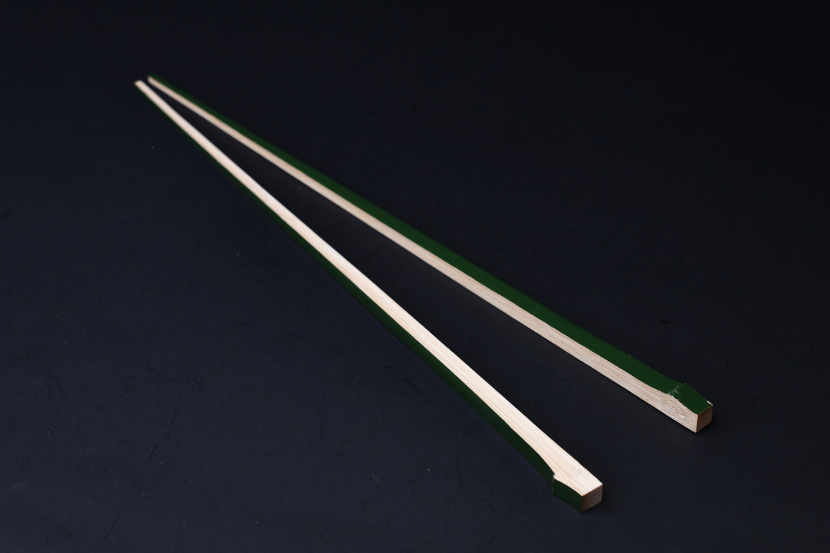 Tenbushi dark green bamboo chopsticks laid full length on black, showing green lacquer stripe along natural bamboo