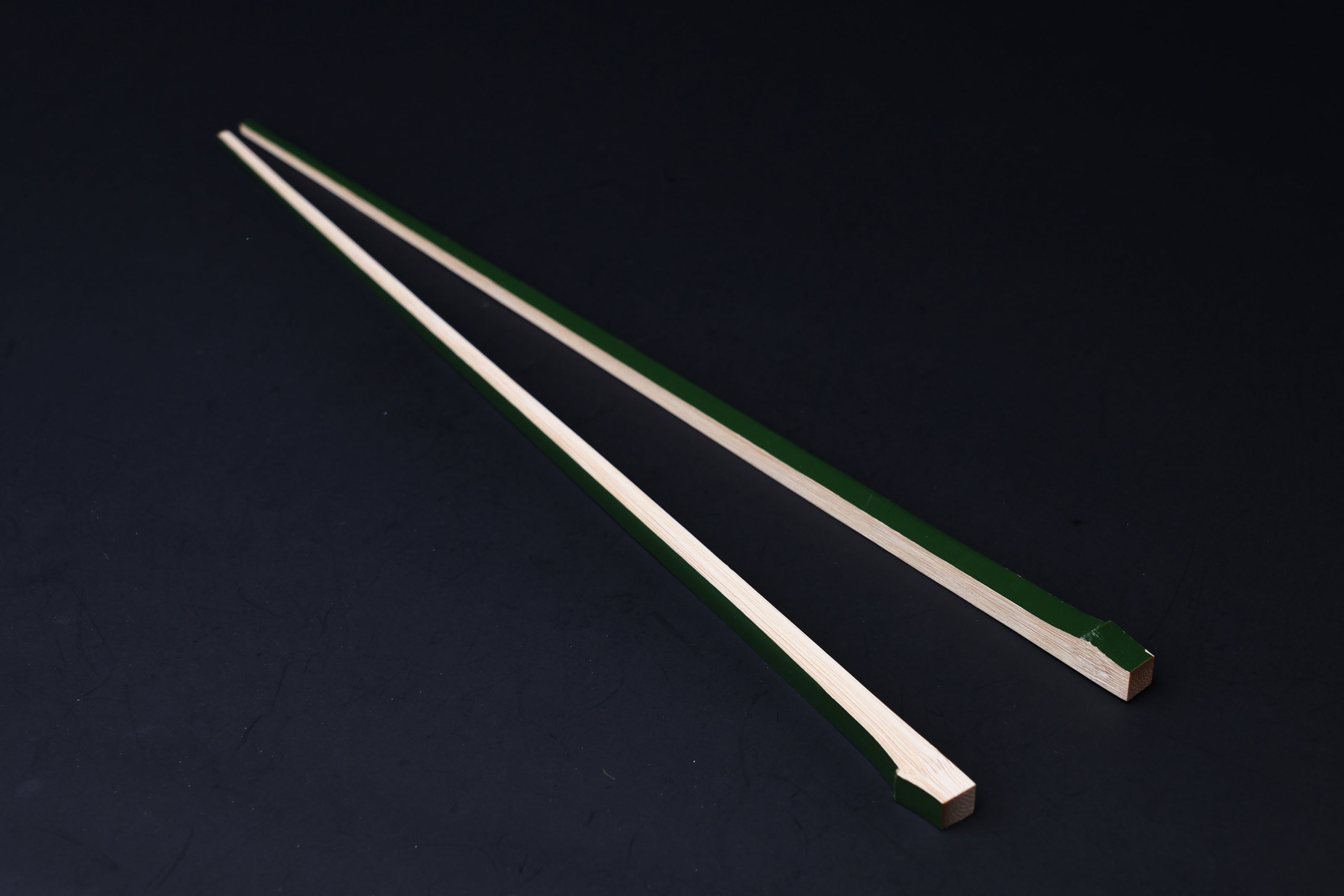 Tenbushi dark green bamboo chopsticks laid full length on black, showing green lacquer stripe along natural bamboo