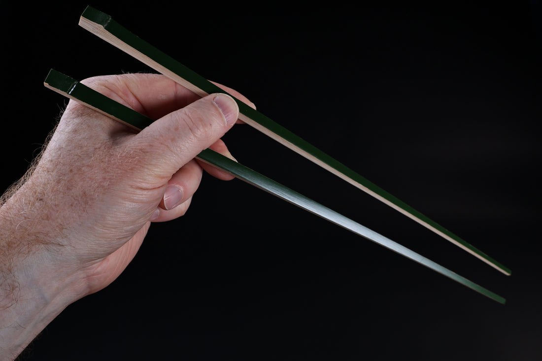 Tenbushi dark green bamboo chopsticks held in hand in cooking grip position against black background