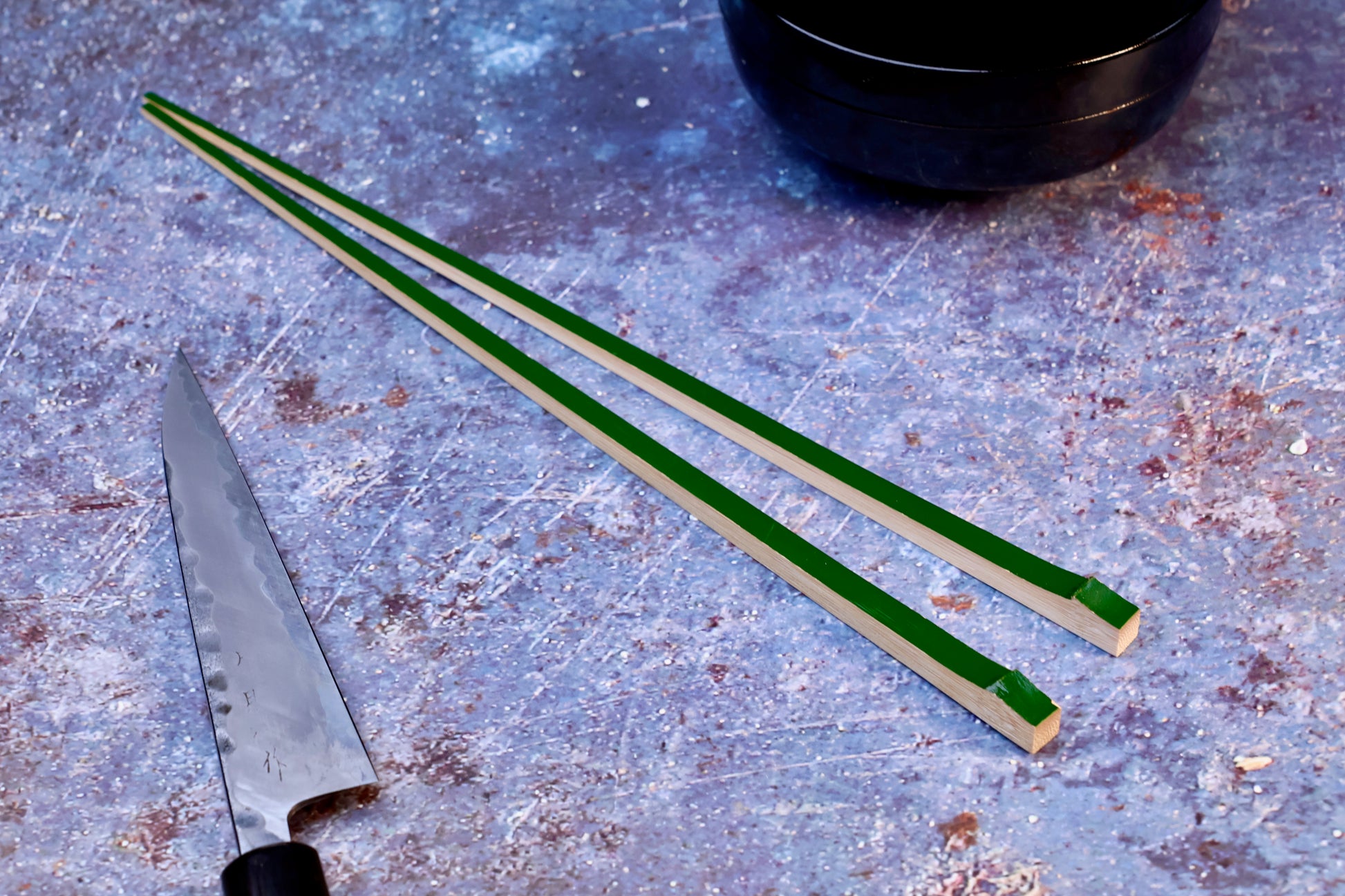 Tenbushi dark green bamboo chopsticks on textured surface with Japanese knife and lacquer bowl, styled kitchen scene
