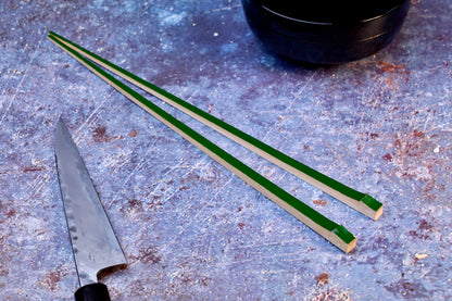 Tenbushi dark green bamboo chopsticks on textured surface with Japanese knife and lacquer bowl, styled kitchen scene