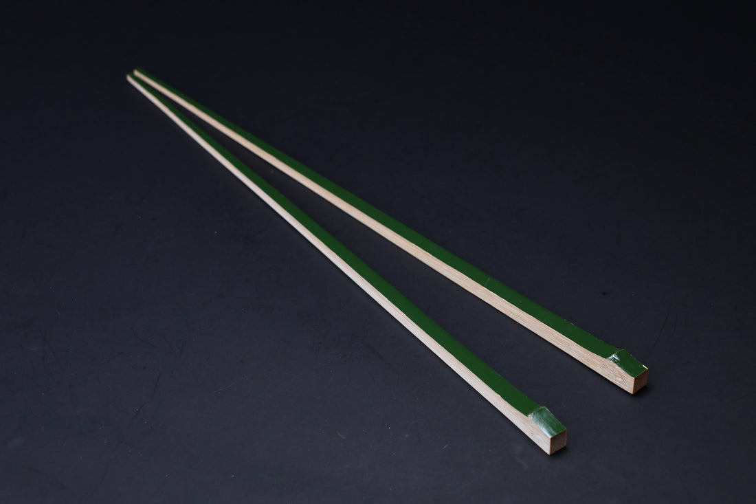 Tenbushi dark green bamboo chopsticks angled on black, square lacquered ends and tapered natural bamboo tips visible