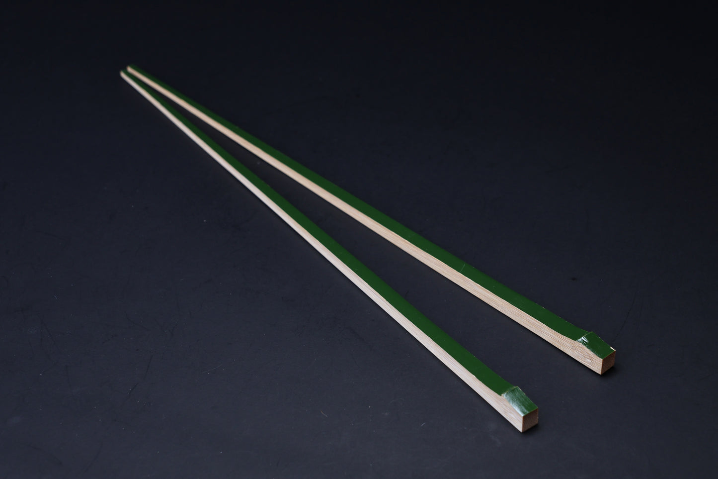 Tenbushi dark green bamboo chopsticks angled on black, square lacquered ends and tapered natural bamboo tips visible