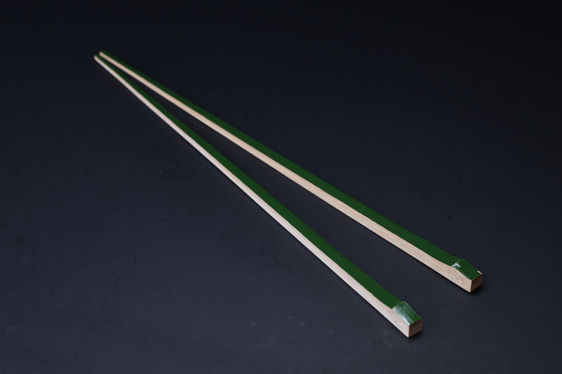 Tenbushi dark green bamboo chopsticks angled on black, square lacquered ends and tapered natural bamboo tips visible