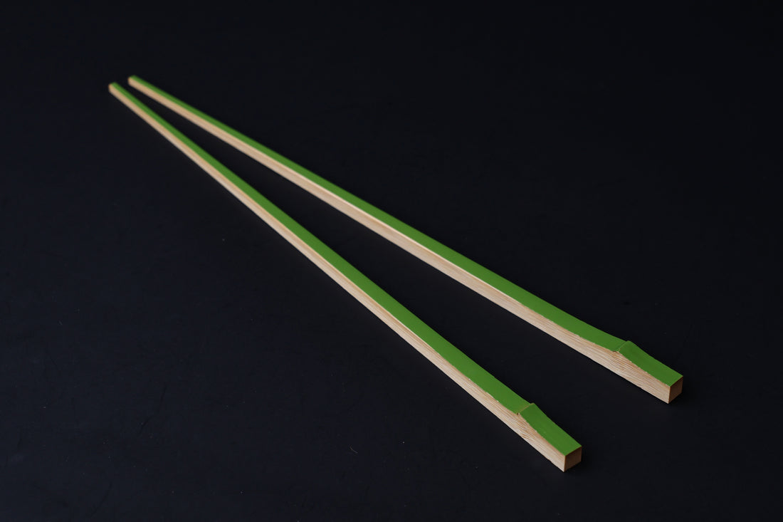 Tenbushi light green bamboo chopsticks laid full length on black, showing green lacquer stripe along natural bamboo