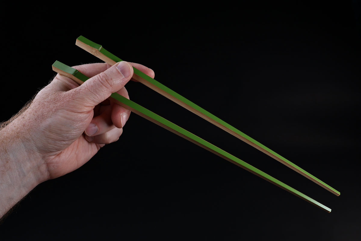 Tenbushi light green bamboo chopsticks held in hand in cooking grip position against black background