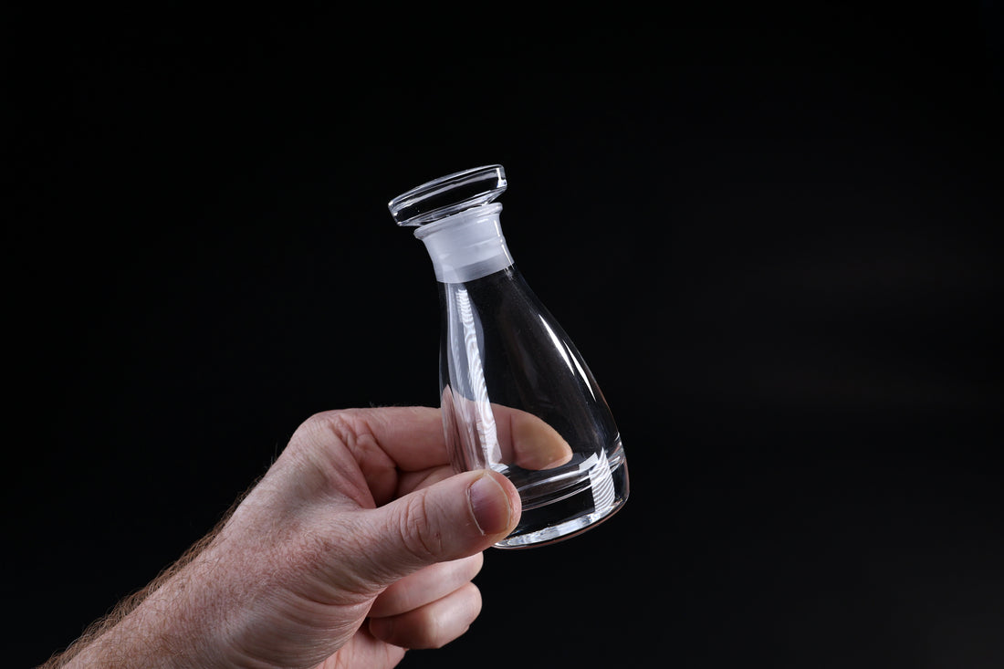 THE Soy Sauce Cruet — hand holding glass cruet showing conical form and stopper detail
