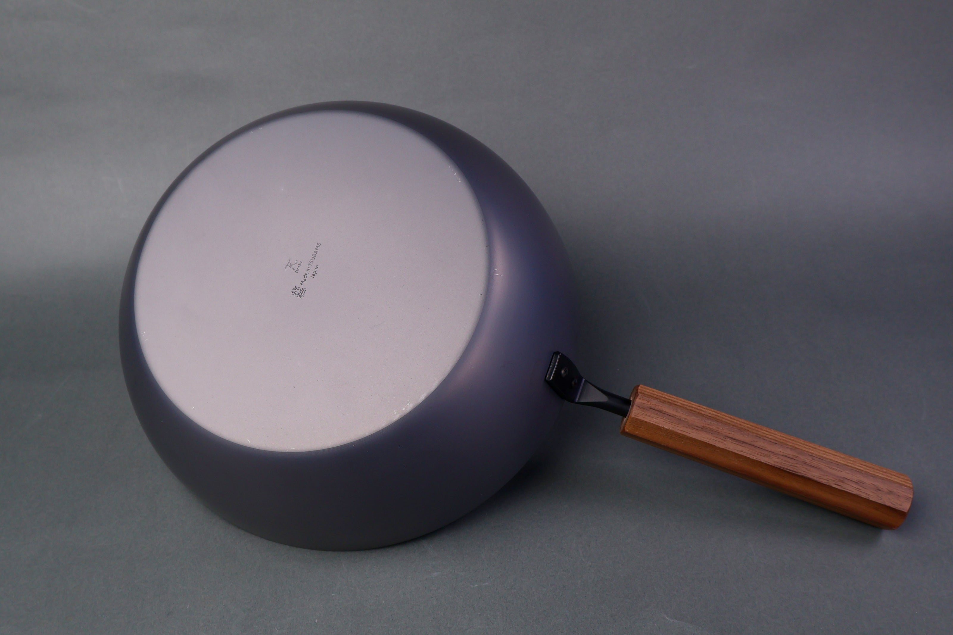 underside of bluish black deep carbon steel frypan long wood handle in grey backdrop