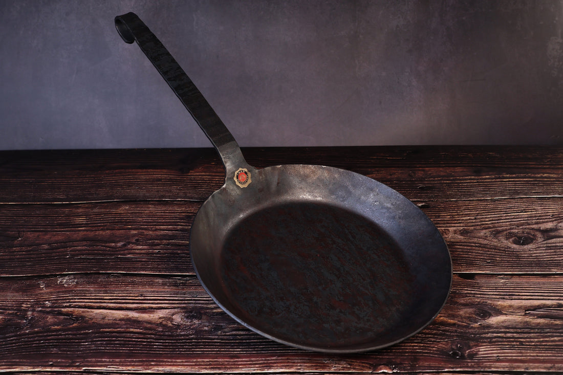 Turk hand-forged iron frying pan with its long hooked handle and brass quality seal, seen from the front