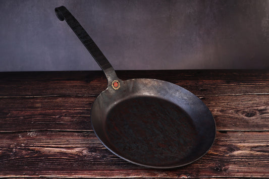 Turk hand-forged iron frying pan with its long hooked handle and brass quality seal, seen from the front