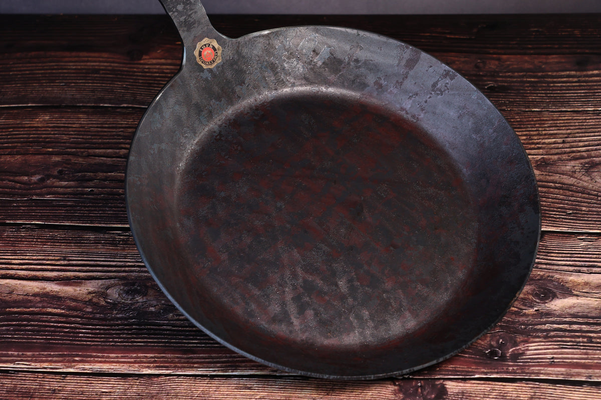 Overhead view of the Turk hand-forged iron frying pan with the cooking surface and brass quality seal visible