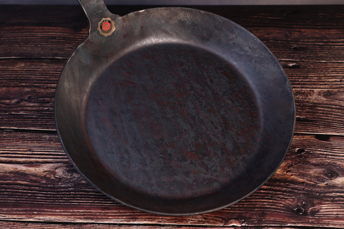 Overhead view of the Turk hand-forged iron frying pan with the cooking surface and brass quality seal visible