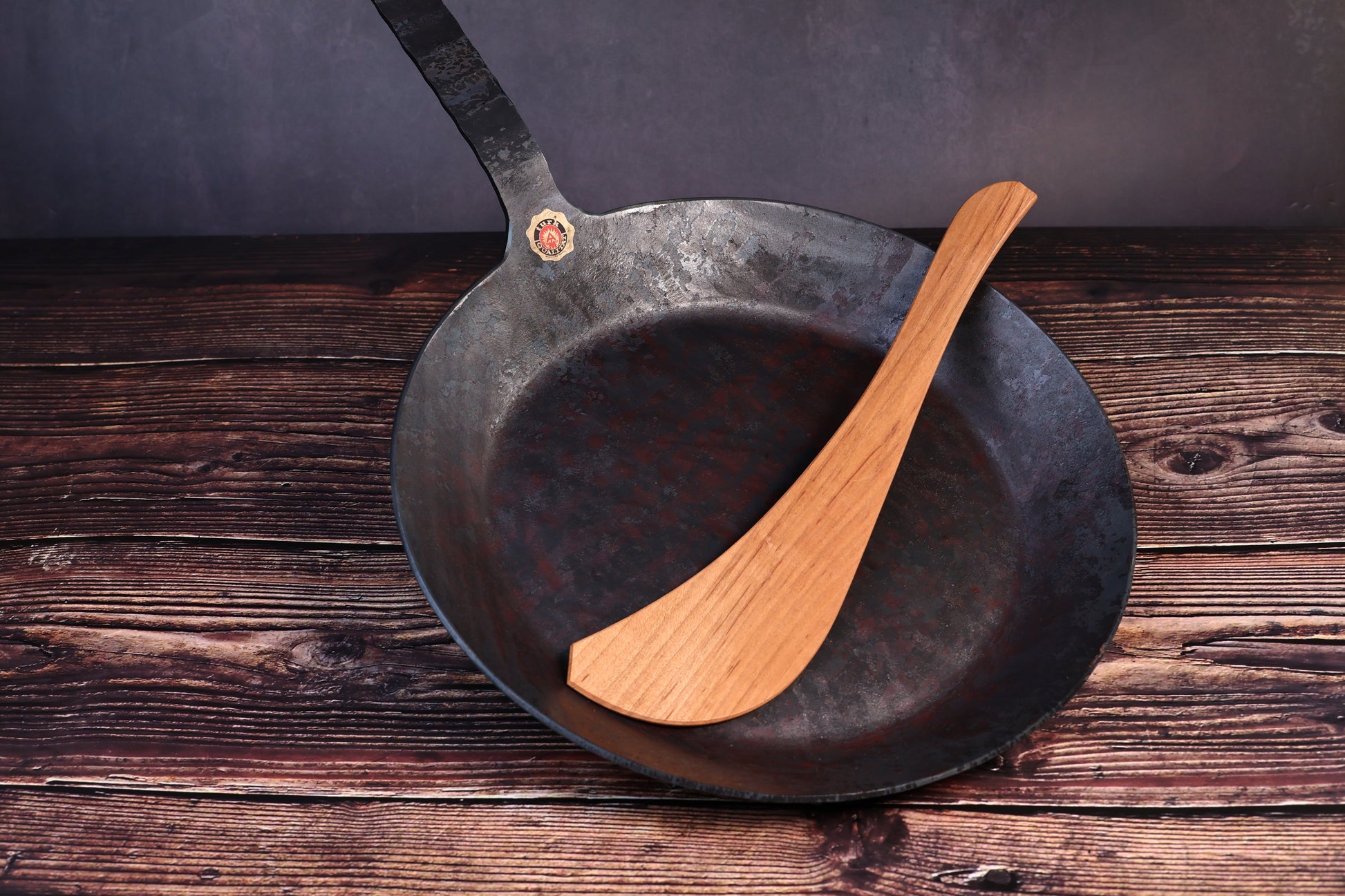 Turk hand-forged iron frying pan with a wooden cooking turner resting inside the bowl
