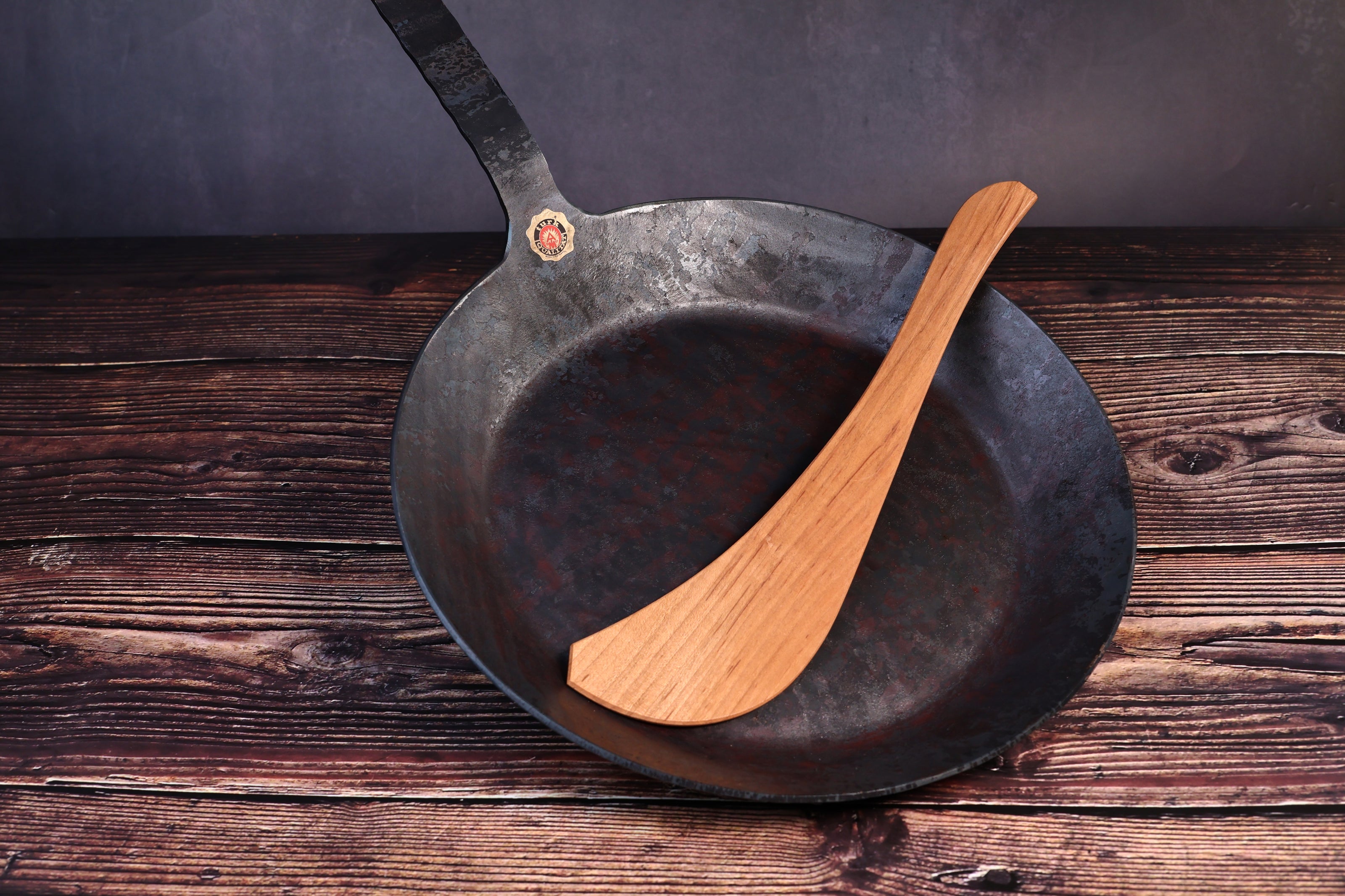 Turk hand-forged iron frying pan with a wooden cooking turner resting inside the bowl