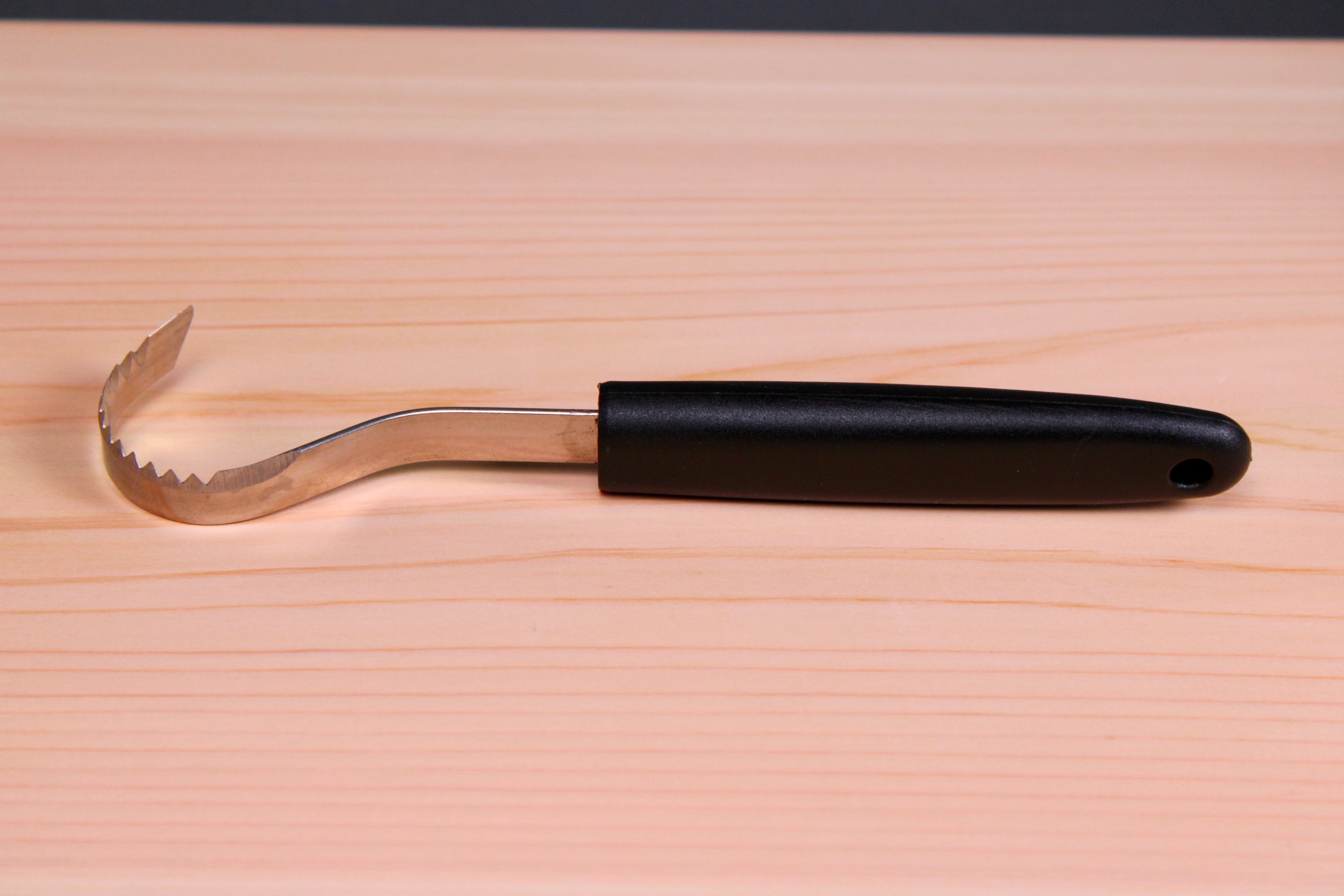 long thin black plastic handled stainless steel curved serrated tool butter curler on hinoki wood board