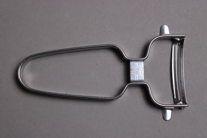 stainless steel vegetable peeler with curved blade wide grip shown on grey background