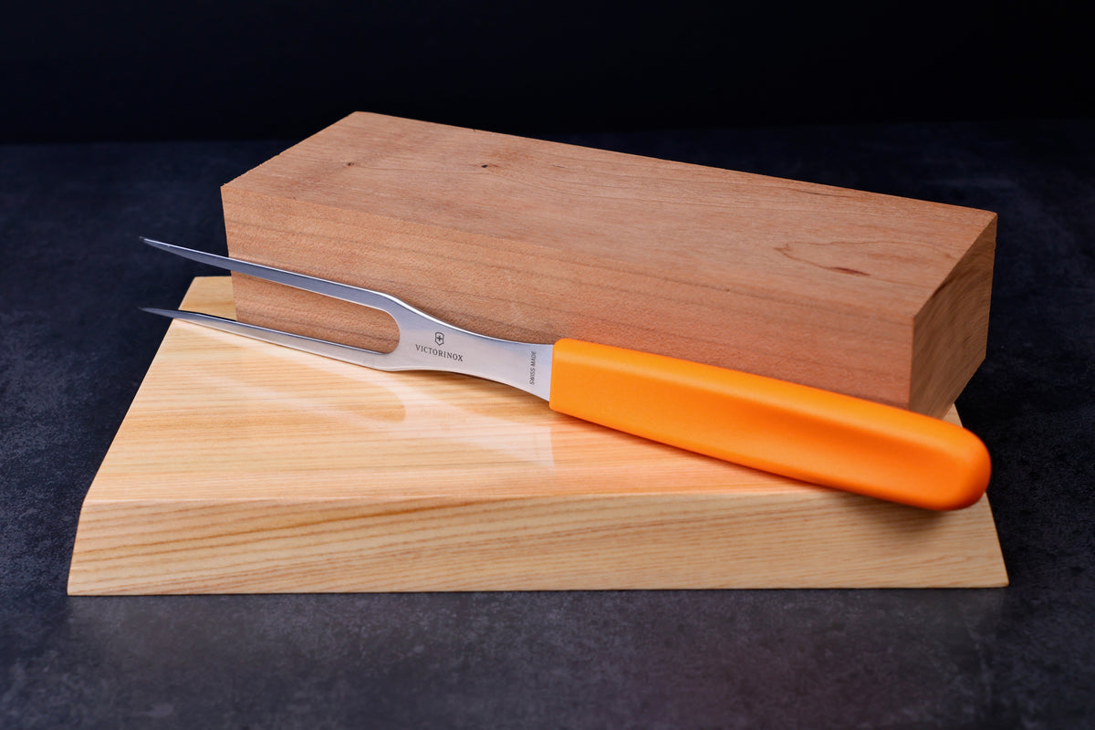 Victorinox Swiss Classic carving fork — full side view showing tines, stamp, and orange handle on wood surface