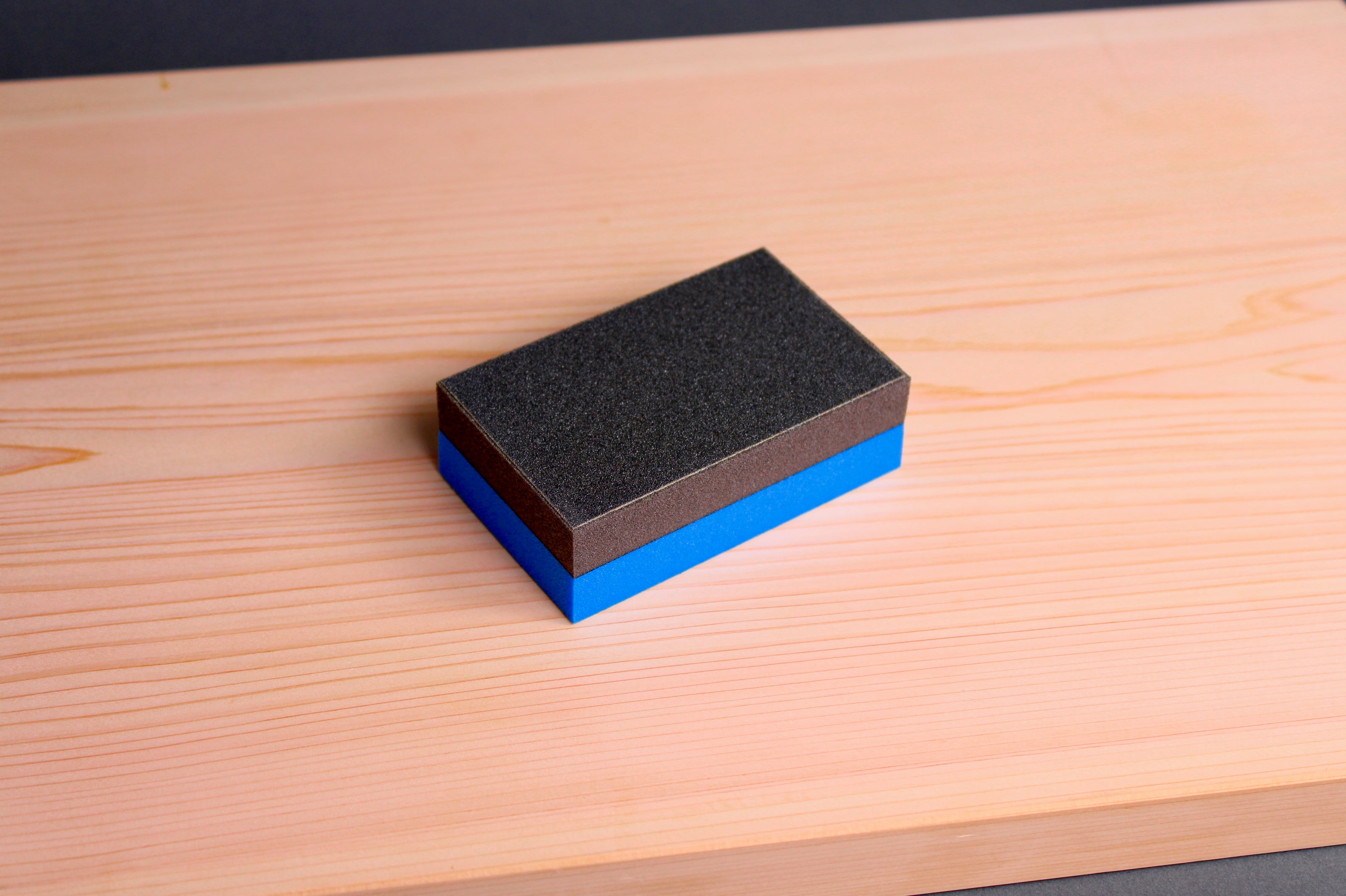 rectangular half black half blue cutting board scrapper sitting atop hinoki wood cutting board with dark backdrop
