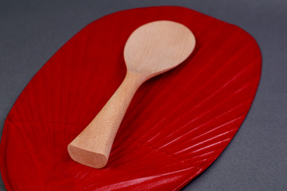 hand carved wooden rice paddle light golden brown yellowish tone of paddle atop deep red background surface