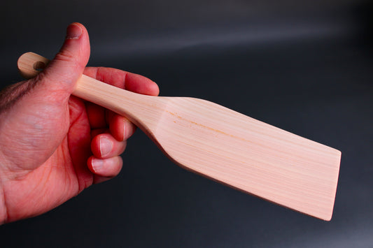 hand holding hinoki wood spatula long wide with thin handle and broad spatula area on dark grey surface