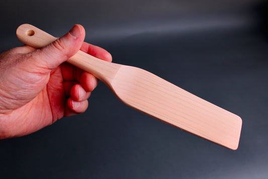 hand holding small hinoki wood spatula long thin handle and  slightly larger broad spatula area on dark grey background